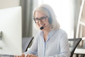 Happy old businesswoman in headset making call looking at computer