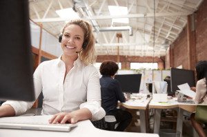 Portrait Of Female Customer Services Agent Working At Desk In Call Center